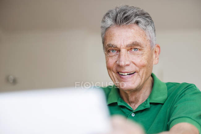 Улыбающийся пожилой человек с помощью цифрового планшета дома — стоковое фото