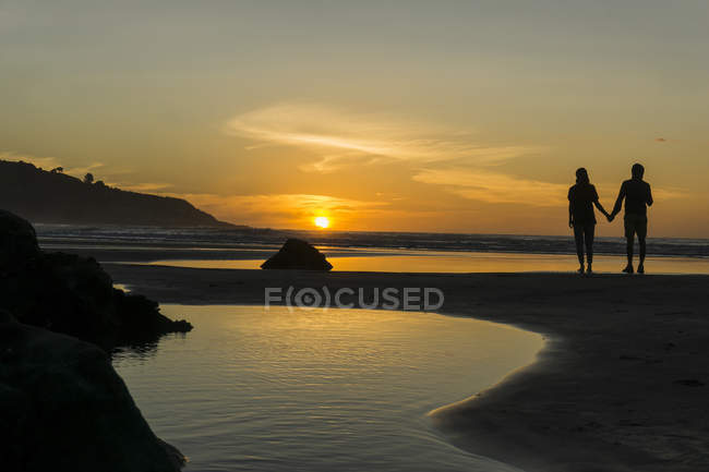 Силует пара стоять рука об руку на пляжі і насолоджуючись захід сонця — стокове фото