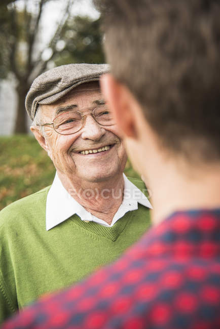 Homem sênior sorrindo para neto adulto no parque — Fotografia de Stock