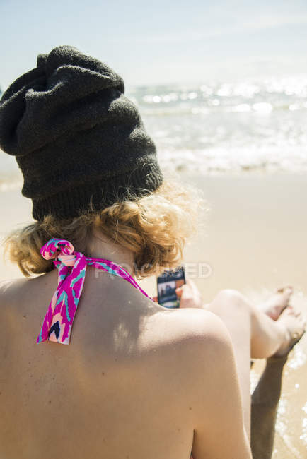 Ragazza adolescente seduta sul lungomare della spiaggia con il suo smartphone — Foto stock