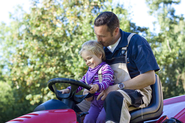 Father and little daughter driving together on lawn mower — Stock Photo