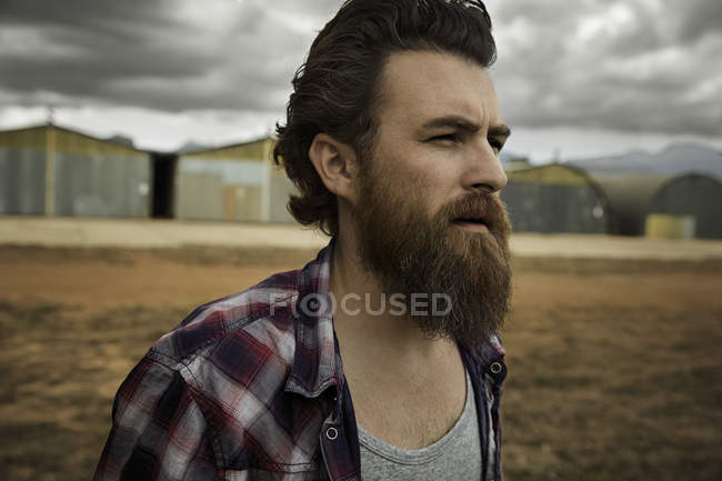 Homme sérieux à la barbe pleine dans un paysage abandonné — Photo de stock