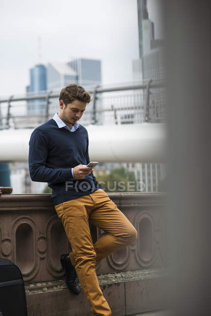 Germany, Hesse, Frankfurt, young man standing on a bridge using smartphone  — watching, city - Stock Photo | #181036350