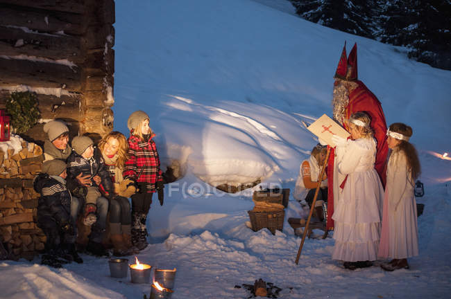 Glückliche Familie mit Engeln und Weihnachtsmann in Holzhütte im Schnee — Stockfoto