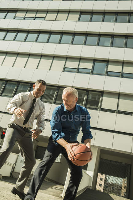 Dos hombres de negocios jugando baloncesto fuera del edificio de oficinas - foto de stock