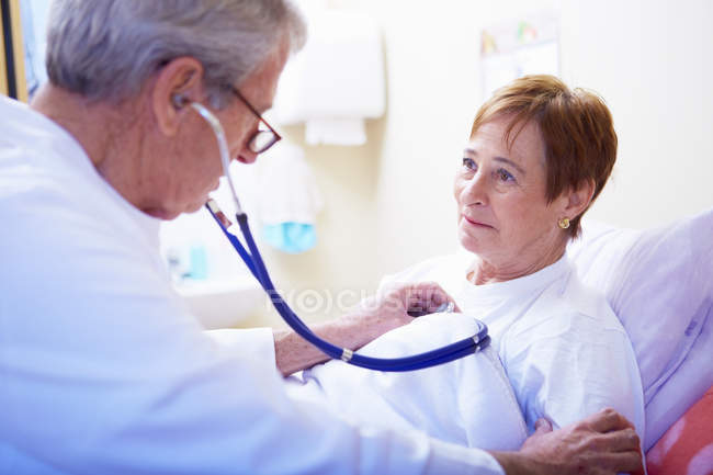 Doctor examining senior woman in hospital bed — Stock Photo