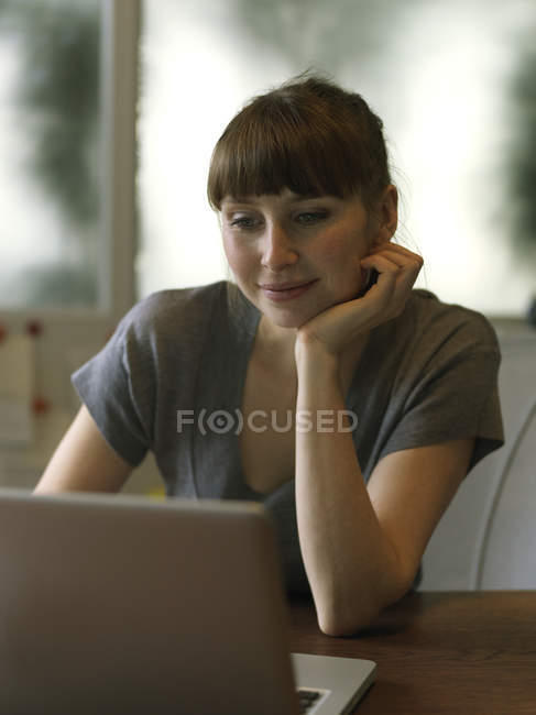 Donna alla scrivania utilizzando il computer portatile guardando lo schermo — Foto stock