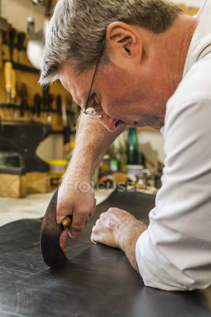 Saddler cutting piece of leather with head knife — Stock Photo