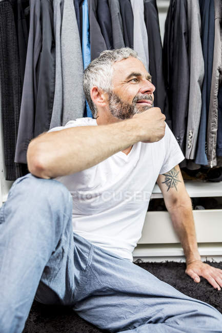 Smiling man sitting on the floor of his walk-in closet — Stock Photo