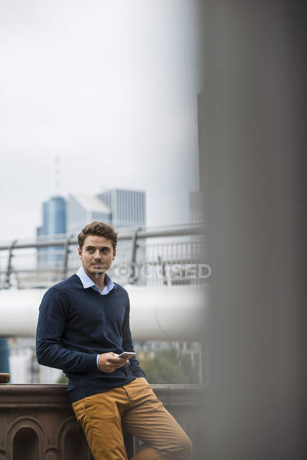 Giovane uomo in piedi su un ponte con il suo smartphone — Foto stock