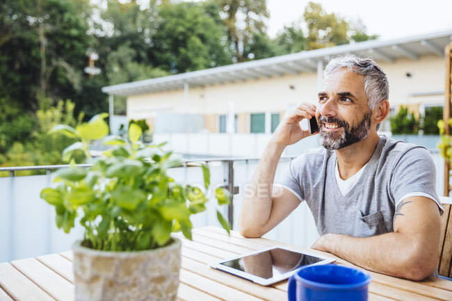 Портрет мужчины, сидящего на балконе и разговаривающего со смартфоном — стоковое фото