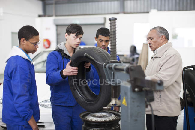 Instructor and trainees adjusting car tire in repair garage — Stock Photo