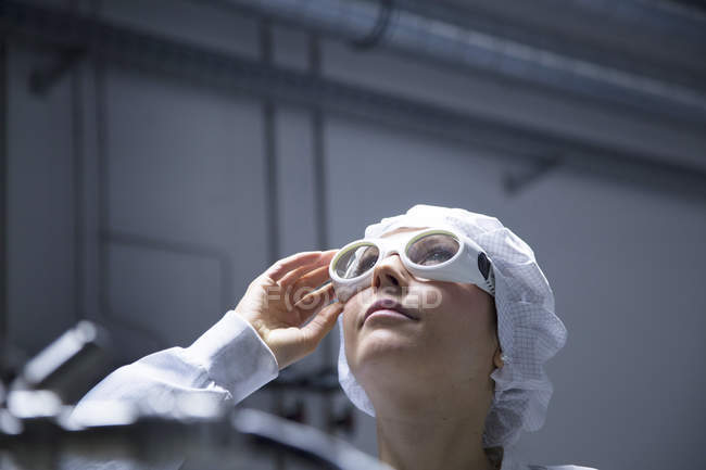 Female technician with protective cap and safety glasses looking up in a laboratory — Stock Photo