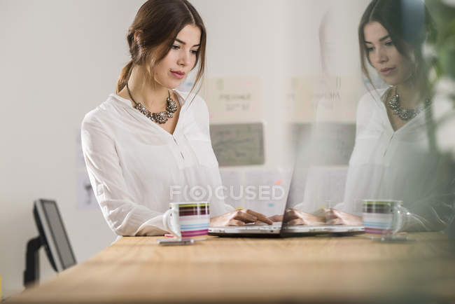 Young businesswoman using laptop in office — Stock Photo