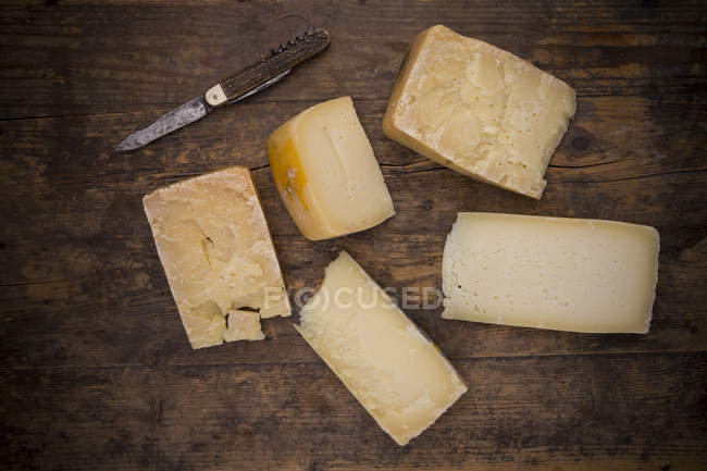 Different pieces of cow milk cheese of Veneto and a pocket knife on dark wood — Stock Photo