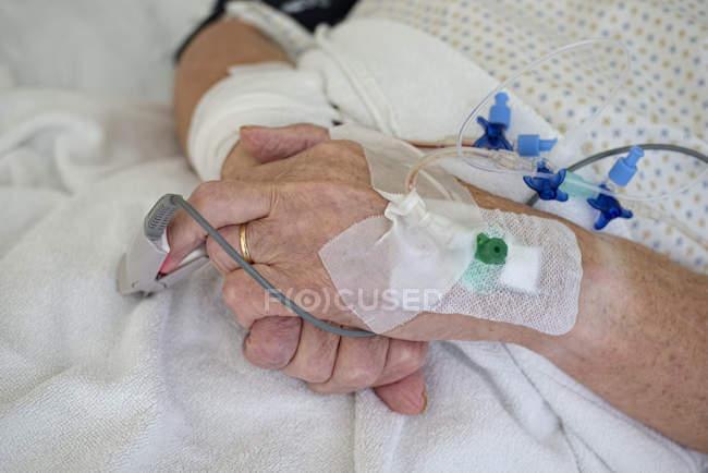 Hands of senior man with cannulae and band-aid being in intensive care — Stock Photo