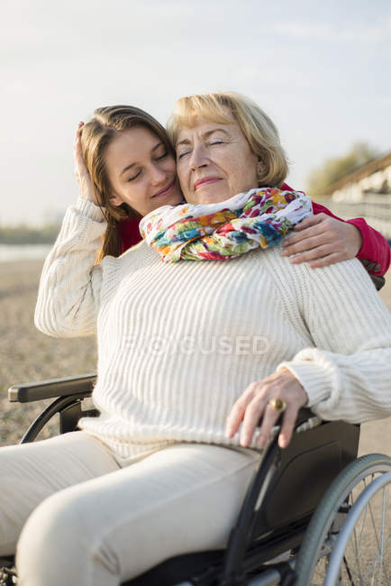 Молодая женщина голова к голове, а ее бабушка сидит в инвалидном кресле — Инвалидноекресло, шарф - Stock Photo