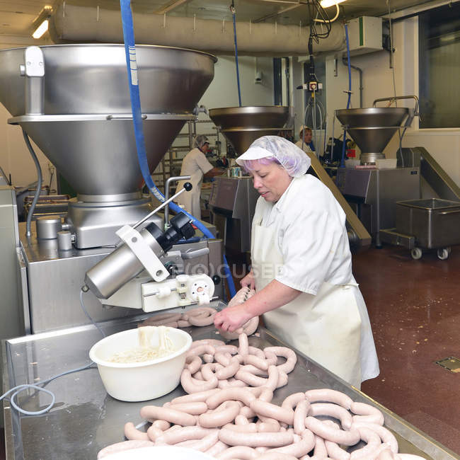 Mature woman working at sausage production in a butchery — Stock Photo