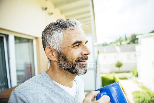 Retrato de homem sorridente relaxante com xícara de café em sua varanda — Fotografia de Stock