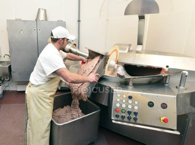 Hombre sacando carne de salchicha de un cortador silencioso en una carnicería - foto de stock