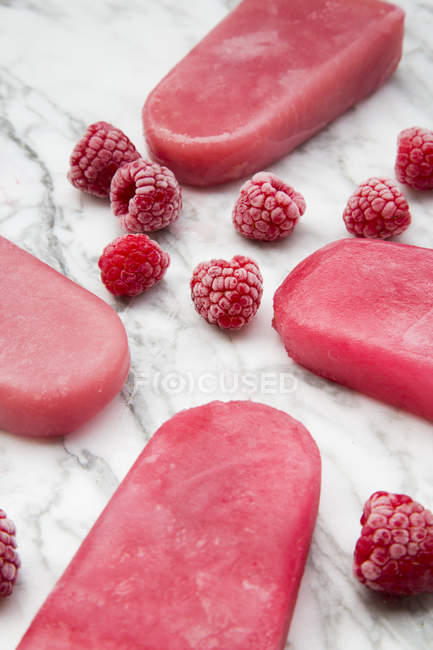 Raspberry ice lollies and frozen raspberries on marble — Stock Photo