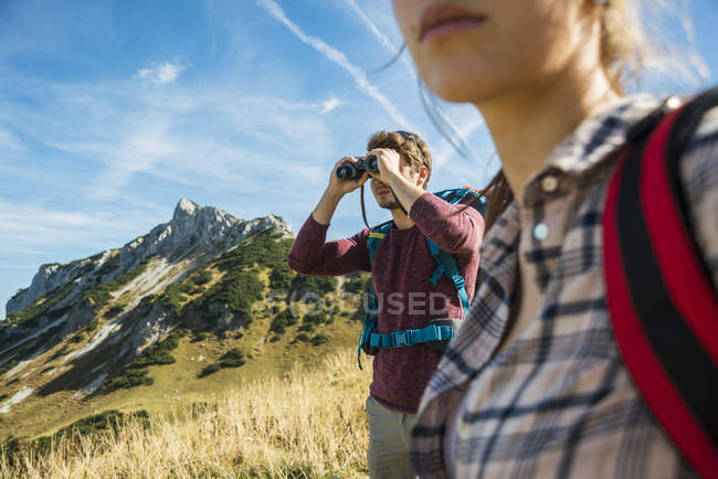 Austria, Tyrol, Tannheimer Tal, young man on hiking trip looking through binocular — Stock Photo
