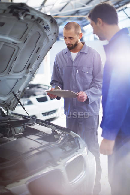 Two car mechanics at work in repair garage standing by the car — Stock Photo