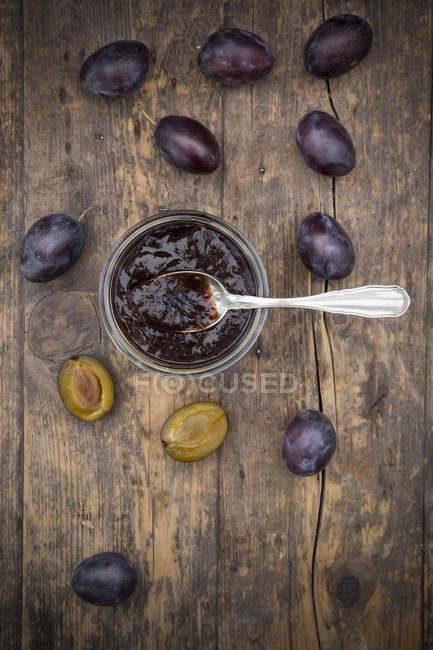 Jar of plum jam and fresh whole and halved plums on dark wood — Stock Photo