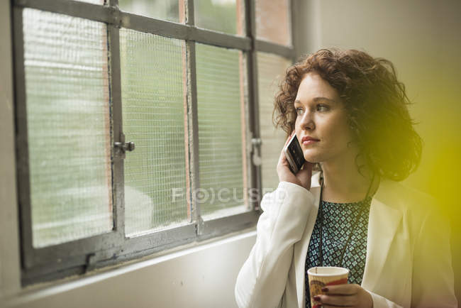 Junge Geschäftsfrau am Handy schaut aus dem Fenster — Stockfoto