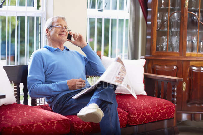 Senior man on the phone reading newspaper at home — Stock Photo