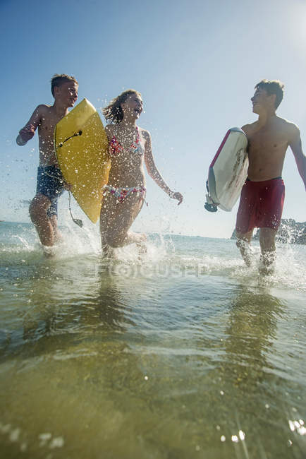 Tre adolescenti con tavole da surf che corrono sul lungomare del mare — Foto stock