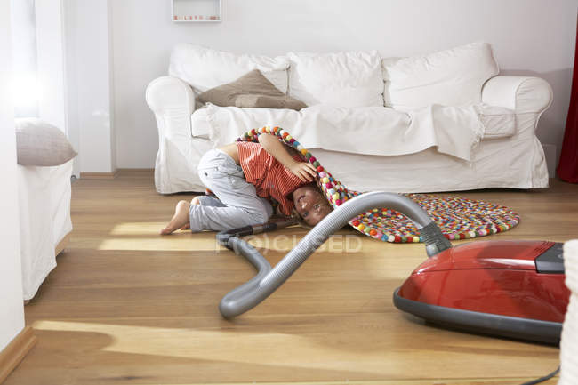 Мальчик в гостиной пылесосит под ковром — стоковое фото