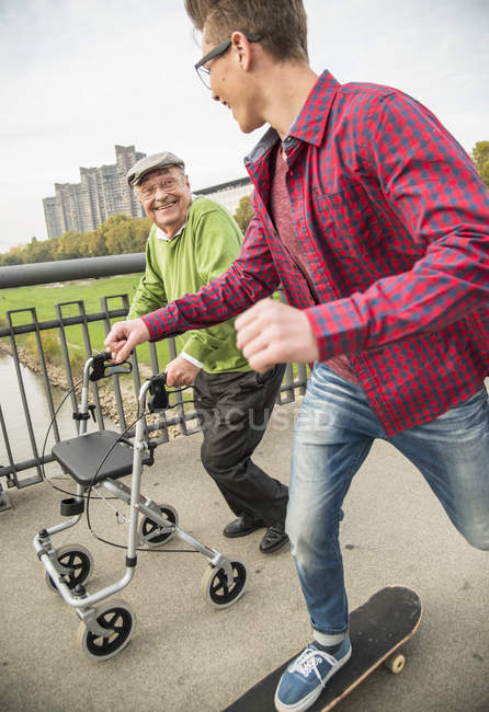 Happy senior man with wheeled walker and grandson with skateboard on street — Stock Photo