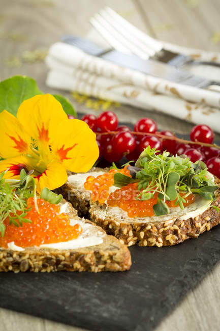 Slices of wholemeal bread with butter and red caviar on slate — Stock Photo