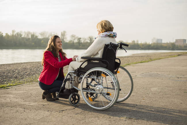 Взрослая внучка помогает бабушке сидеть в инвалидном кресле — стоковое фото