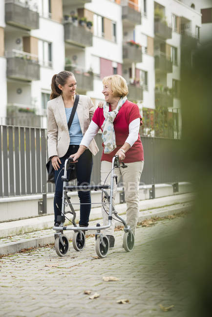 Adult granddaughter assisting her grandmother walking with wheeled walker — Stock Photo