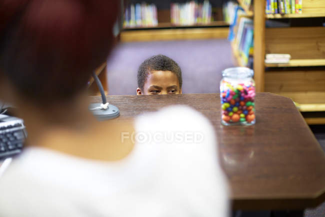 Menino na biblioteca espreitando o frasco de doces — Fotografia de Stock
