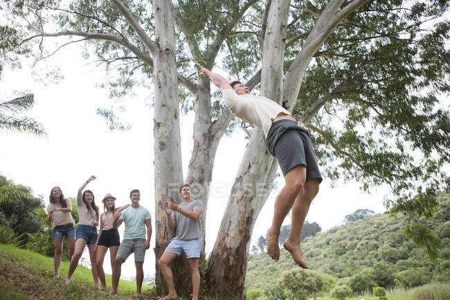 Gruppo di amici tifo mentre l'uomo oscillare su un albero — Foto stock