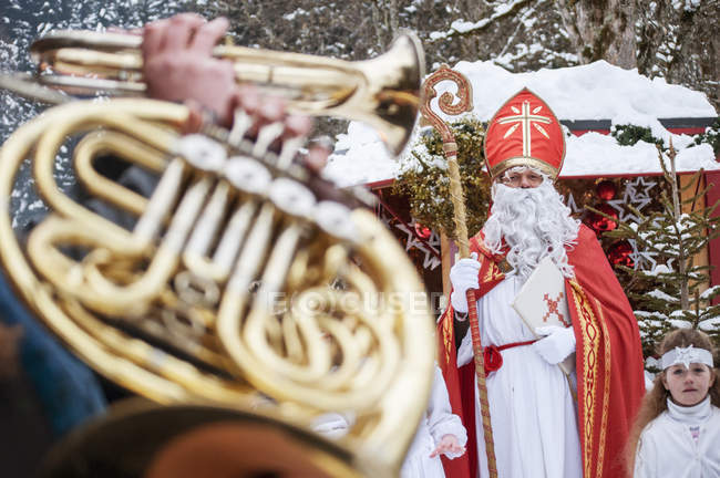 Musician playing horn with angel and Santa Claus in background — Stock Photo