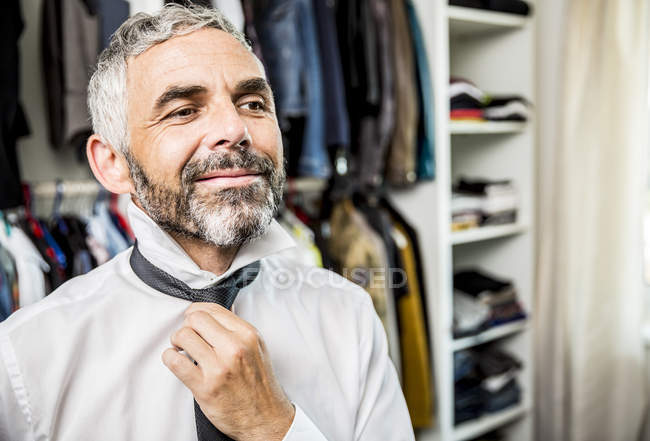 Портрет улыбающегося бизнесмена, связывающего галстук в его гардеробной — стоковое фото