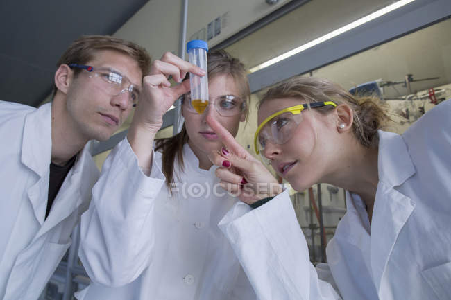 Trois chimistes travaillant dans un laboratoire chimique regardant une éprouvette — Photo de stock