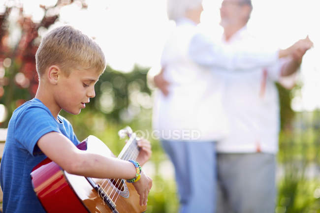 Nipote che suona la chitarra con coppia anziana che balla nel parco — Foto stock