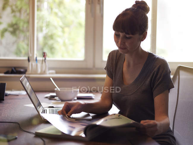 Жінка за столом з журналом для читання ноутбуків — стокове фото