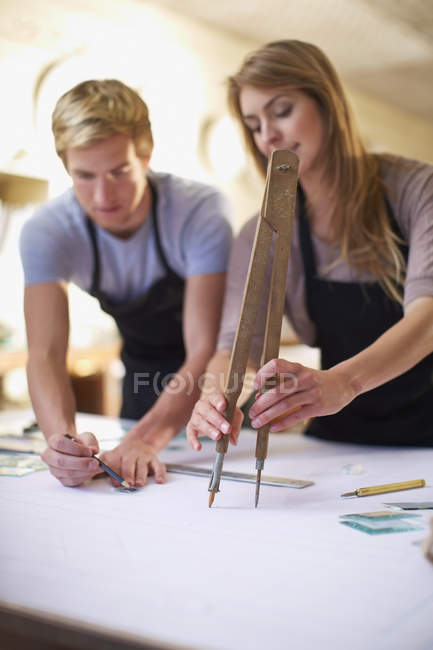 Couple in a workshop manufacturing stained glass with large compasses — Stock Photo