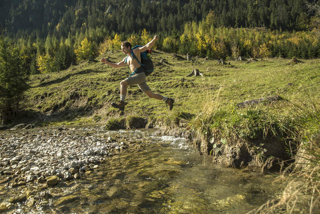Austria, Tirol, Tannheimer Tal, joven excursionista cruzando el agua - foto de stock