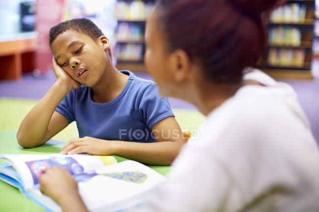 Young teacher and reluctant boy at table — Stock Photo