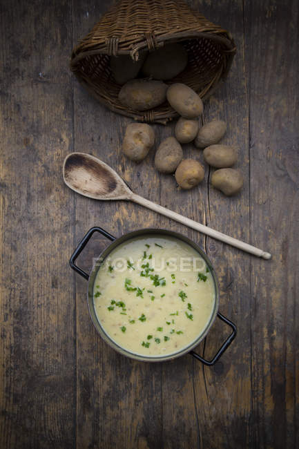 Pentola di zuppa di patate guarnita con erba cipollina, cucchiaio di legno e patate su legno scuro — Foto stock