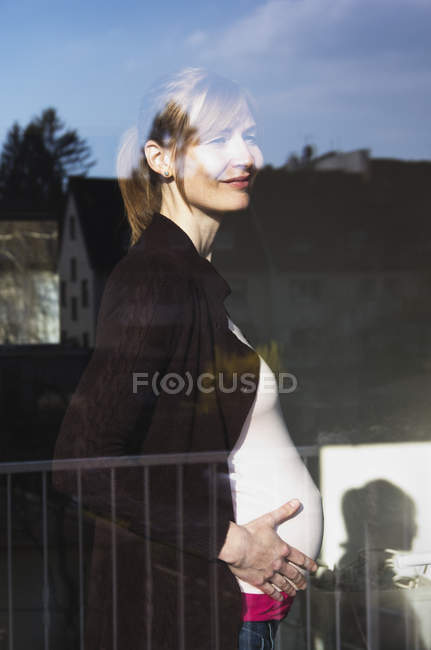 Femme enceinte regardant par la fenêtre — Photo de stock