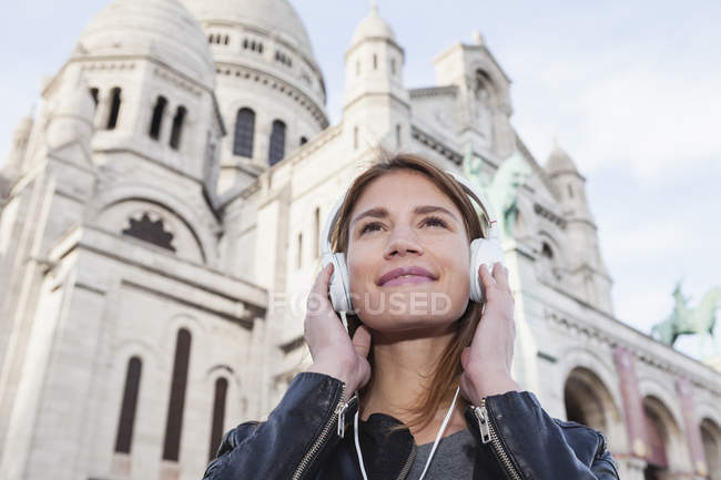 Frankreich, paris, porträt einer glücklichen jungen frau, die mit kopfhörern vor sacre coeur musik hört — Stockfoto