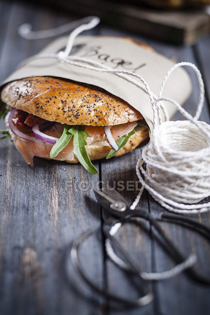 Dos bagels caseros adornados envueltos en papel, cuerda y tijeras sobre madera gris - foto de stock